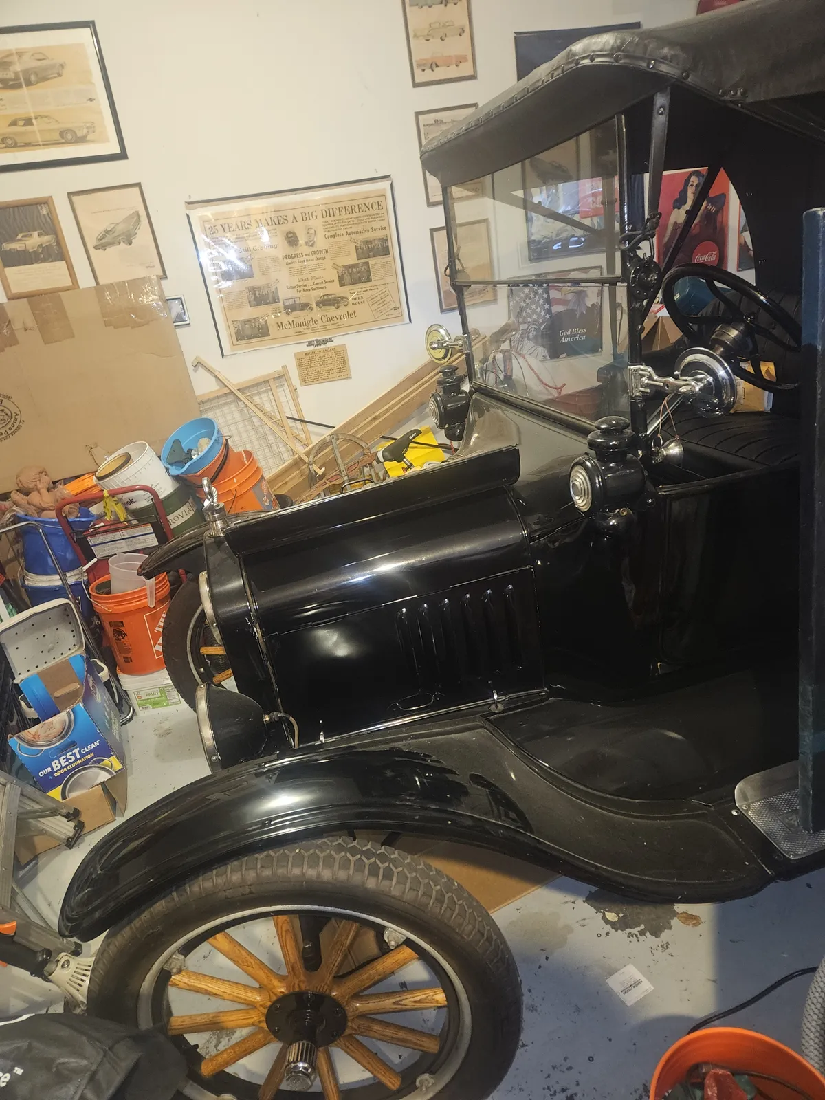 Antique black car with wooden spoke wheels being worked on inside a shop