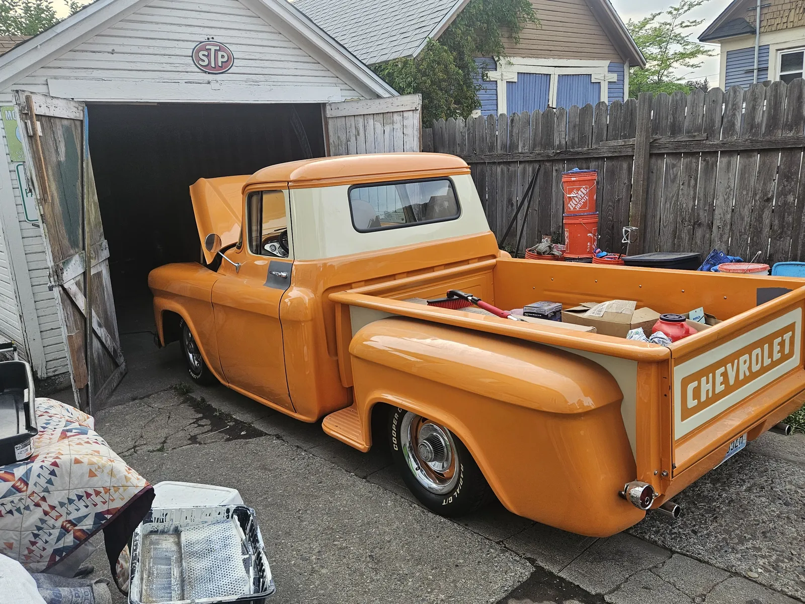 Orange 1960s Chevrolet pickup truck parked outside a garage during a build