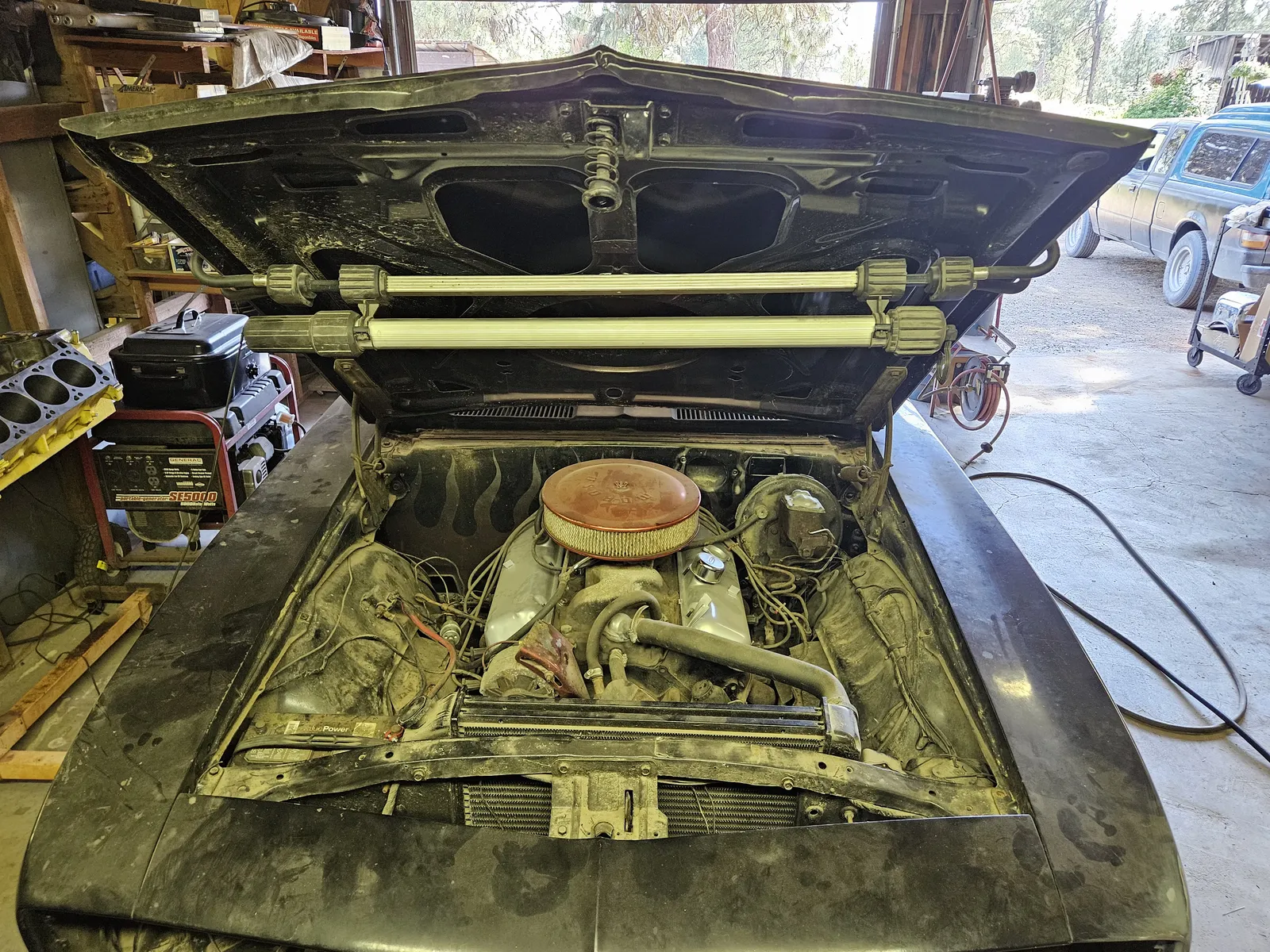 Classic car engine bay opened up on a shop floor for a carburetor swap