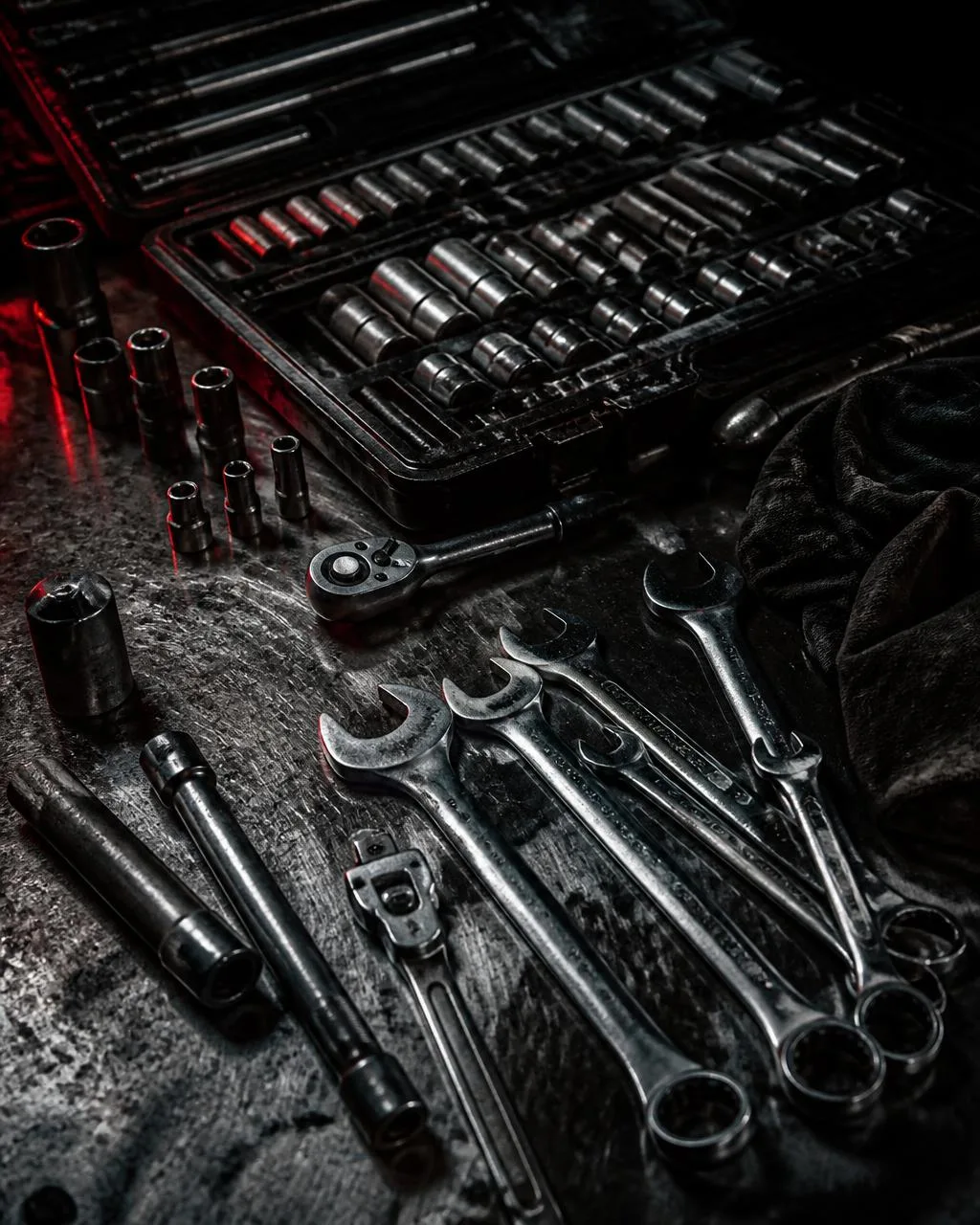 Worn socket set and chrome wrenches laid out on a dark steel workbench